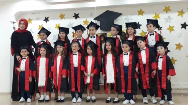 Sahnede kırmızı bantlı kiralık kep-cübbelerle ilkokul mezuniyet töreni