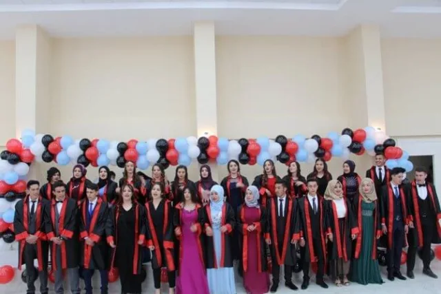 Balonlu salonda kırmızı bantlı kiralık cübbelerle lise mezuniyet töreni