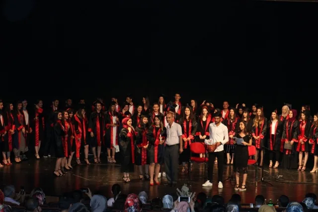 Sahnede kırmızı bantlı kiralık mezuniyet cübbeleriyle gece töreni